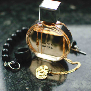 Elegante Chance von Chanel Parfümflasche in goldenem Farbton, daneben schwarze Perlenarmband und goldene Schmuckkette auf dunkler Marmoroberfläche in stimmungsvoller Produktfotografie