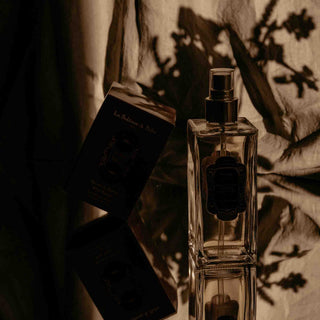 "Elegante Parfümflasche mit schwarzem Etikett neben ihrer Verpackung in einer stimmungsvollen Schattenspiel-Atmosphäre, fotografiert in warmen, dunklen Sepia-Tönen mit künstlerischer Beleuchtung