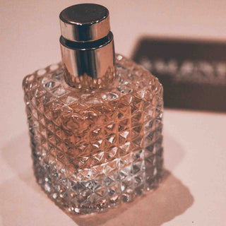 Elegante Parfümflasche aus geschliffenem Kristallglas mit geometrischem Muster und silbernem Sprühkopf in warmer, rosafarbener Beleuchtung auf hellem Hintergrund