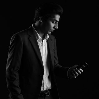 Geschäftsmann in dunklem Anzug betrachtet sein Mobiltelefon im stilvollen Schwarz-Weiß-Portrait