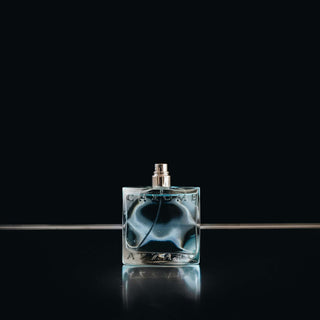 Elegantes Parfümflakon aus Glas mit blauem Duft auf schwarzem Hintergrund mit Spiegelung, minimalistisches Produktfoto im Studio-Setup