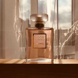 Coco Mademoiselle Chanel Parfum Flakon in warmen Sonnenlicht auf einer Holzoberfläche vor einem hellen Fenster, luxuriöses Parfüm in eleganter Glasflasche mit goldenem Label